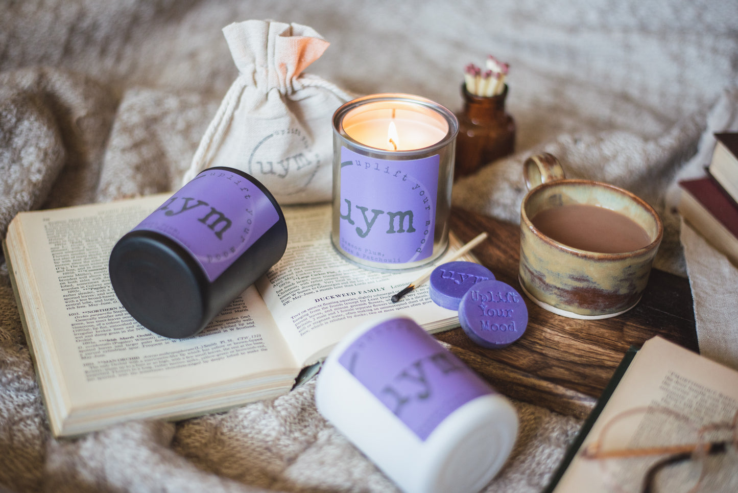 Damson Plum, Rose & Patchouli Candles, highly sceted natural wax, organic cotton wick, metallic tin lighted candle, matt black, matt white glass jar candles, cosy background. Uplift Your Mood Scents