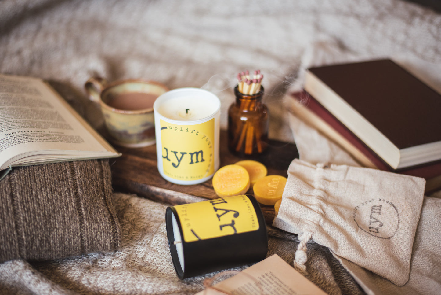 Thai Lime and Mango natural wax candle,matt black candle, matt white glass jar candle unlighted, natural wax melts yellow in a cotton bag, books and a nice cup of tea, cosy atmosphere, Uplift Your Mood Scents